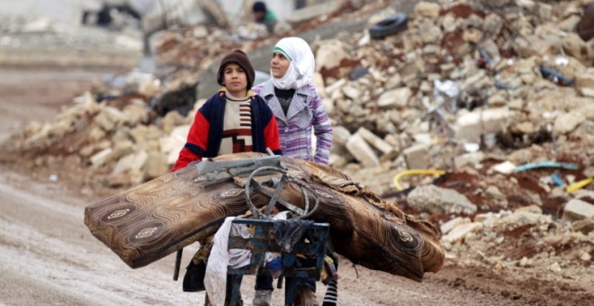 Samah, 11, y su hermano Ibrahim transportan sus pertenencias salvadas de su casa destrozada por la guerra en Alepo. / REUTERS