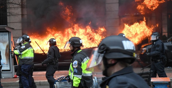 Los manifestantes queman un coche durante la comitiva presidencial de Donald Trump. - REUTERS