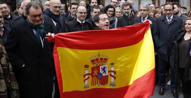 Un hombre despliega una bandera española ante la presencia de Francesc Homs y de Artur Mas en el paseo hacia el Tribunal Supremo. /EFE