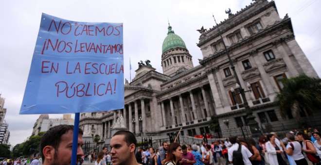 Un manifestante sostiene un letrero que dice: 'No caemos en la escuela pública' frente al Congreso después de la gafe de ayer del presidente argentino Mauricio Macri sobre los argentinos que 'caen en la escuela pública' durante una protesta en Buenos Aire