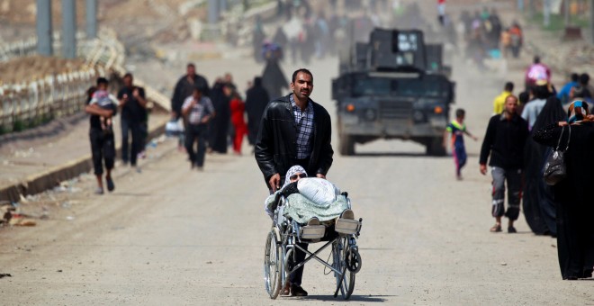 Un desplazado iraquí de Mosul por los combates entre el Ejército y el Estado Islámico lleva a una mujer en silla de ruedas.-REUTERS/Khalid al Mousily
