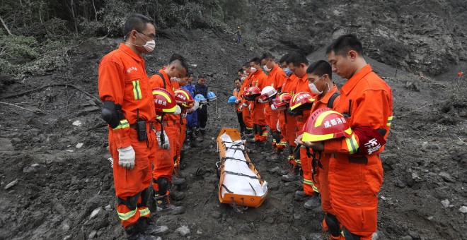 Trabajadores de rescate chinos rinden un minuto de silencio ante el cuerpo de una de las victimas del alud que sepultó una aldea del Tibet./REUTERS
