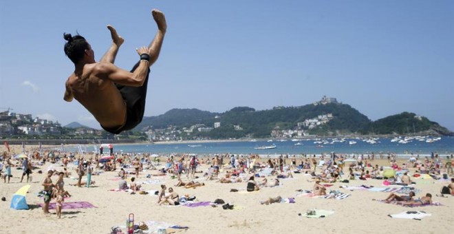 Un joven realiza un salto acrobático hoy en la playa de La Concha de San Sebastián, donde tras las lluvias ha vuelto el tiempo veraniego./EFE