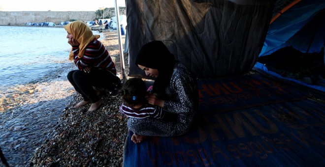 Faten (i), procedente de Siria, se sienta a la orilla del mar junto a su nuera, cerca de su tienda en el campo de refugiados de Souda, en la isla de Chios. 'Está tardando demasiado. Esta lentitud para traer a toda la familia me asusta', dice Faten. 'No te