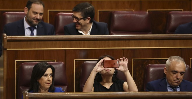 La diputada socialista Adriana Lastra, toma fotos con su móvil del hemicíclo del Congreso de los Diputados. A la izquierda, la portavoz del PSOE, margarita Robles y a la derecha, Rafael Simancas. EFE/Mariscal