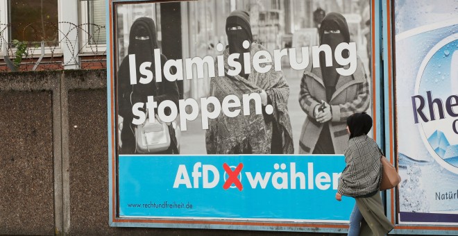 Una mujer con un pañuela en la cabeza camina por delante de uno de los carteles de campaña de Alternativa por Alemania (AfD) en Marxloh, un barrio de Duisburgo conocido por acoger a una mayoría turca entre sus residentes. 13 de septiembre del 2017. REUTER