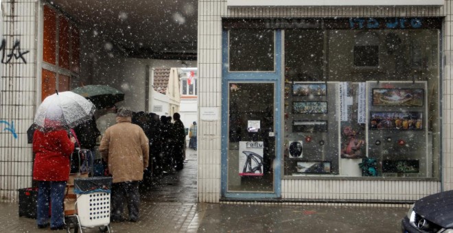 Varias personas guardan cola para recoger alimentos mientras nieva en la ciudad de Dortmund./REUTERS