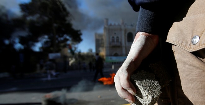 Un palestino sujeta una piedra mientras mira los disturbios con las fuerzas de seguridad israelíes.REUTERS/Mussa Qawasma