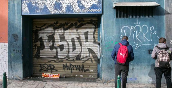 Unos jóvenes miran la puerta del bar Tocadiscos en Zaragoza. | JAVIER CEBOLLADA (EFE)