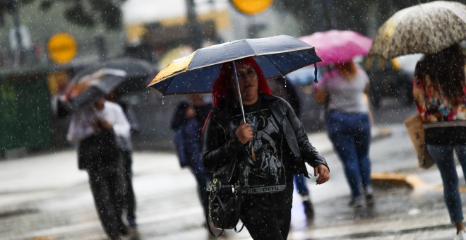 Una mujer cruza un paso de peatones durante una fuerte tormenta, en el centro de Buenos Aires (Argentina). EFE/David Fernández