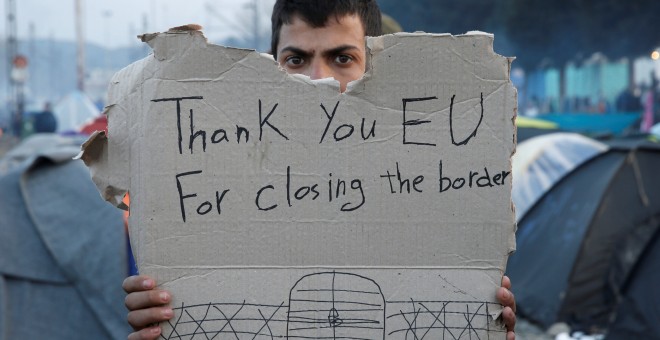 Un refugiado sostiene un cartel con mensaje en un campamento improvisado en la frontera entre Grecia y Macedonia. / Reuters