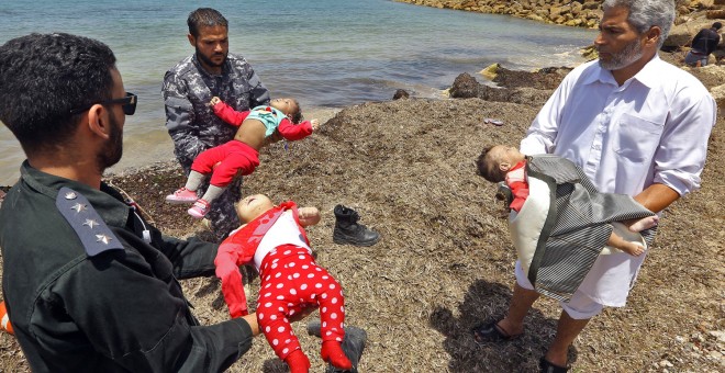Guardacostas libios sostienes los cadáveres de tres bebés fallecidos en el naufragio frente a las costas libias. Hay cien desaparecidos y 16 supervivientes.- AFP/ MAHMUD TURKIA