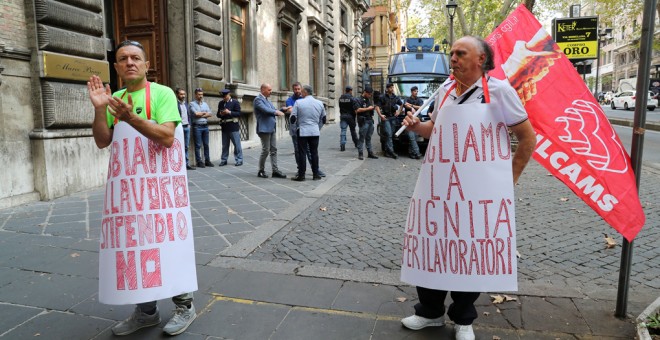 Dos personas protestan frente al Ministerio de Trabajo italianl, en Roma, con sendas pancartas que dicen 'Queremos dignidad para los trabajadores' y 'Tenemos trabajo, pero no sueldo'. REUTERS/Tony Gentile
