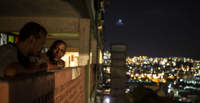 Dos vecinos de uno de los bloques del barrio 23 de Enero de Caracas conversan durante la noche.- JAIRO VARGAS
