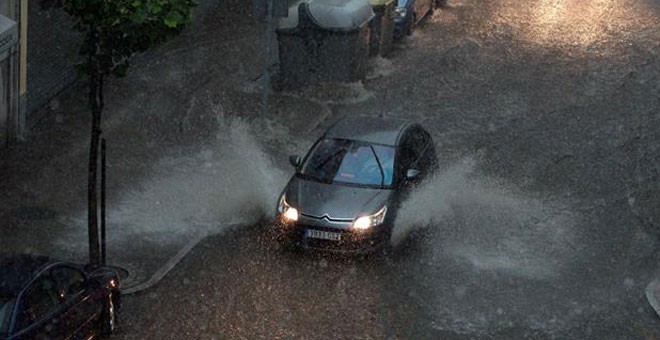 Dos vehículos circulan por una calle inundada en Ourense. / / EFE