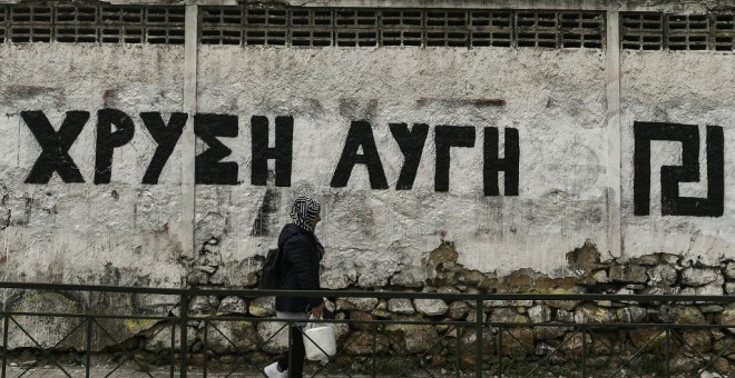 Una mujer pasa junto a una pared pintada con el logotipo del partido neonazi griego Amanecer Dorado, en Atenas. AFP/Aris Messinis
