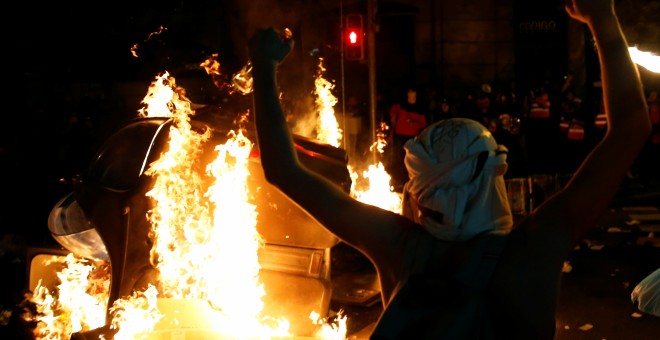 Un encapuchado levanta los brazos ante un contenedor ardiendo en el centro de Barcelona. /REUTERS