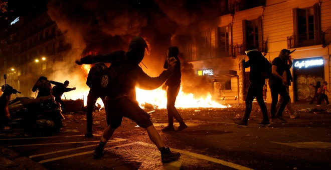 Un grupo de radicales en una barricada incendiada lanzando objetos a los Mossos en Barcelona. /REUTERS