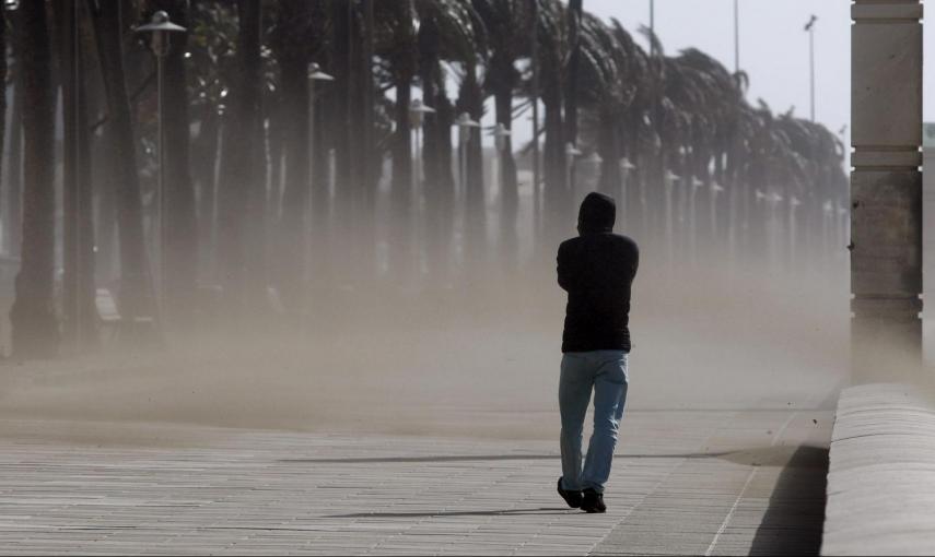 Un hombre camina entre la vetisca de arena por el paseo maritimo de Almeria, provincia que se encuentra en alerta naranja por fuertes vientos. EFE / Carlos Barba