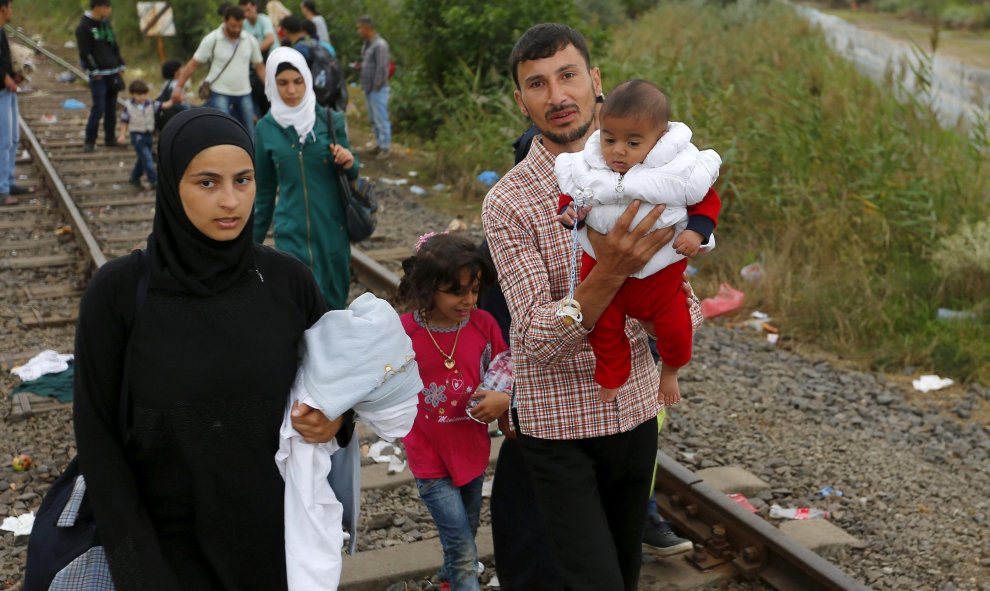Refugiados sirios caminan con sus hijos en brazos a lo largo de una vía de ferrocarril, después de cruzar la frontera húngaro-serbio en Hungría, cerca Röszke, donde se ha construído una alambrada de cuchillas para frenarlos de 175 km de longitud.- REUTERS