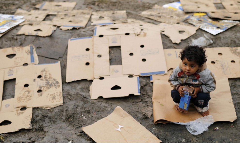 Un niño descalzo encima de un cartón con un paquete de galletas espera mientras los emigrantes esperan entrar en Croacia desde Berkasovo, Serbia. 28 de septiembre de 2015. REUTERS/Antonio Bronic