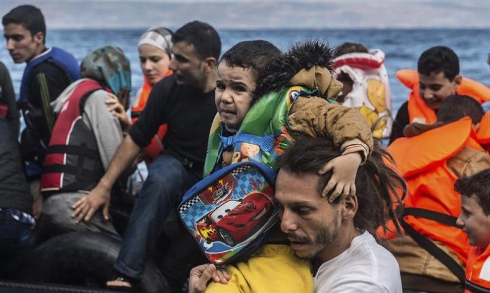 Un voluntario ayuda a un niño refugiado a su llegada a la costa tras una dura travesía en lancha neumática, en la isla de Lesbos (Grecia). Alrededor de 100.000 refugiados y migrantes llegaron a las islas griegas durante el mes de agosto, según datos de la