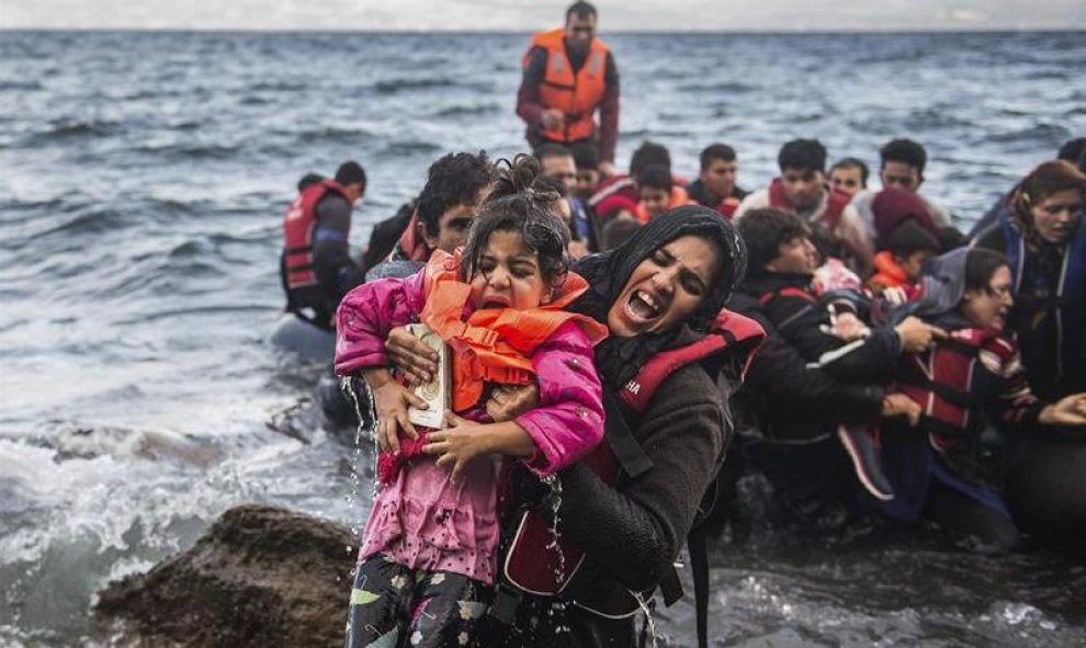 Una refugiada salta de una lancha neumática con su hija en brazos tras alcanzar la costa, en la isla de Lesbos (Grecia). EFE/Filip Singer