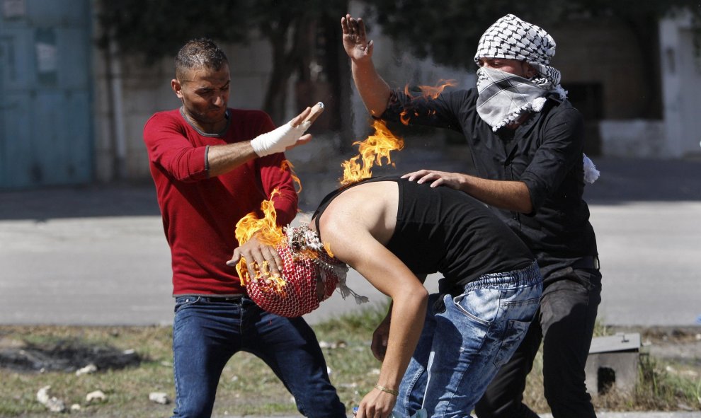 Manifestantes palestinos intentan apagar el fuego que quema a un compañero, originado por un cóctel molotov que él trataba de lanzar hacia las tropas israelíes durante los enfrentamientos en Hebrón, 13 de octubre de 2015. REUTERS / Mussa Qawasma