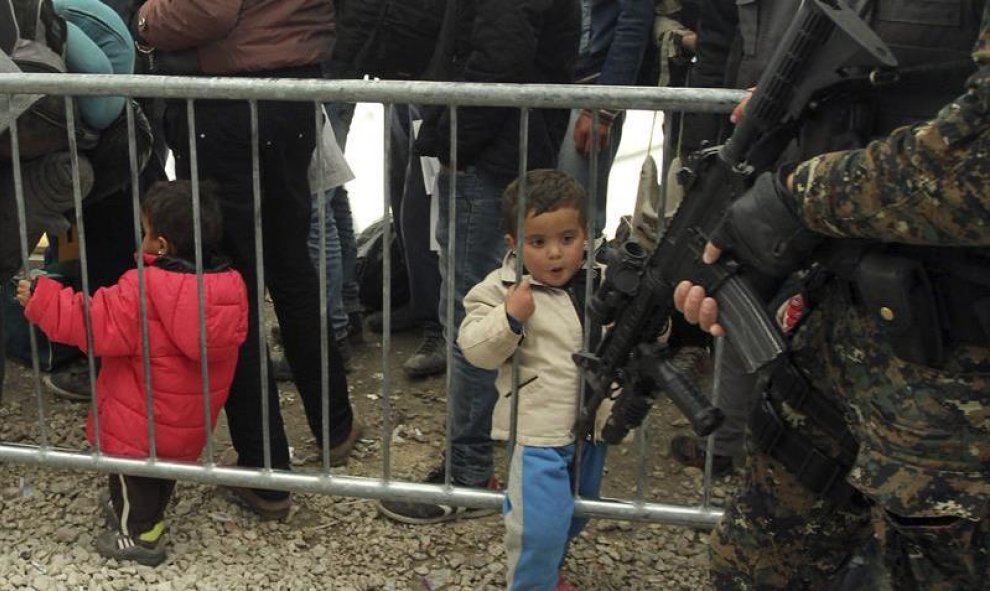 Un niño refugiado contempla el arma de un militar serbio, mientras espera para ser registrados en el campo de refugiados de Presevo, al sur de Serbia. EFE/Djordje Savic