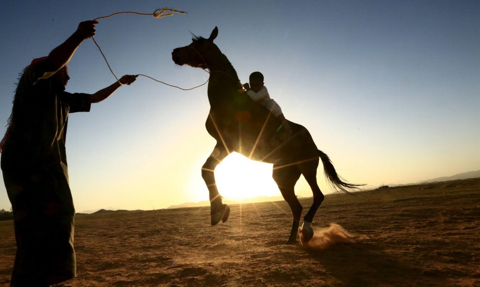 Un hombre saudí enseña a su hijo a montar a caballo en un desierto cerca de Tabuk. REUTERS/Mohamed Al Hwaity