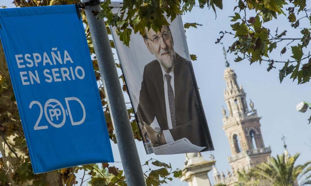 Cartel electoral del PP con la fotografía de Mariano Rajoy, presidente del Gobierno en funciones y candidato a la reelección, que cuelgan de una de las farolas del centro de Sevilla ante La Giralda, durante la campaña electoral para las elecciones general