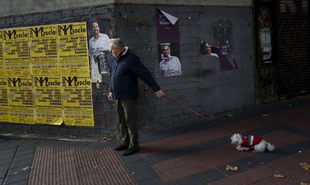 Un hombre pasea a su perro junto a unos carteles de Podemos en Madrid.REUTERS/Susana Vera