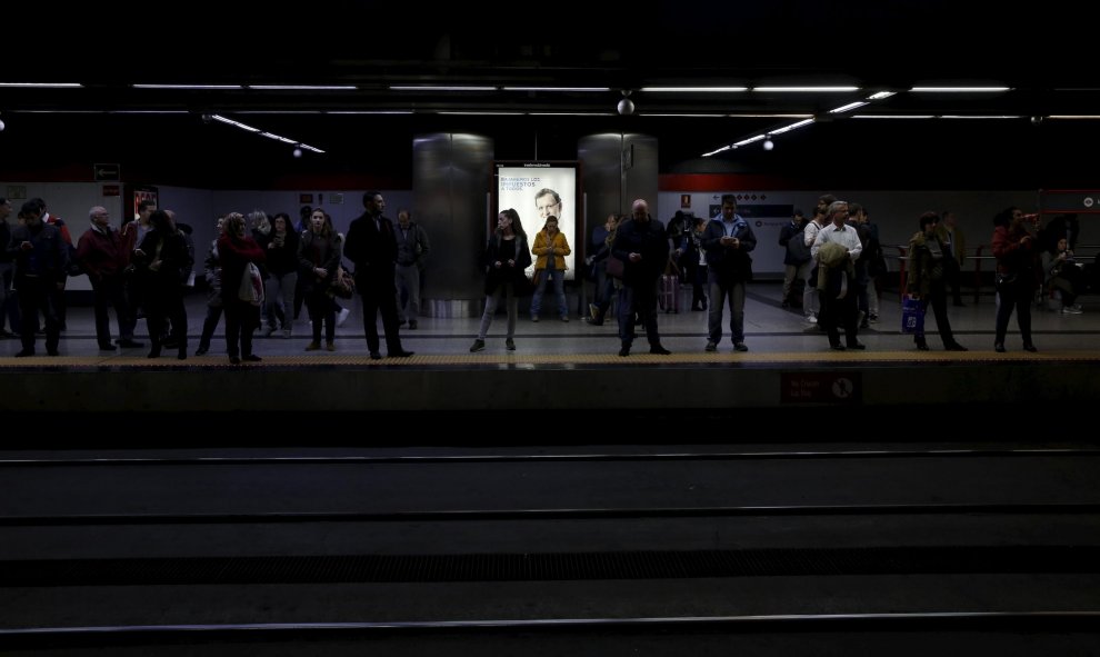 varios pasajeros en el andén de una estación de Cercanías de Madrid, junto a un cartel electoral de Mariano Rajoy para las elecciones del 20-D. REUTERS/Susana Vera