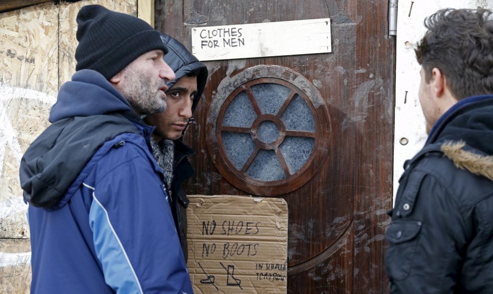 Varios inmigrantes esperan frente a la tienda donde se reparte ropa y calzado en el campamento provisional para refugiados de procedentes de Irak, Kurdistán, Irán y Siria, cerca de Dunkerque (Francia). REUTERS / Pascal Rossignol
