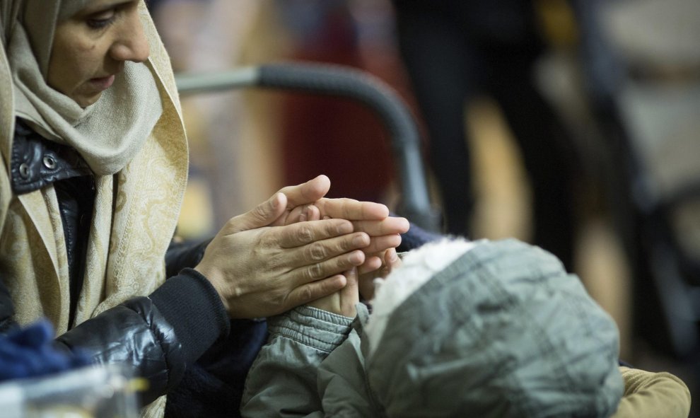 Una mujer calienta las manos de su hijo en una tienda de campaña a las puertas de la Oficina de Sanidad y Asuntos Sociales en Berlín. EFE/KAY NIETFELD