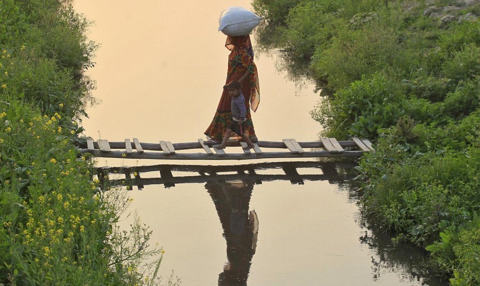 Una mujer agarra la mano de un niño mientras cruzan un puente hecho de bambú en un canal en Allahabad, India. REUTERS/Jitendra Prakash