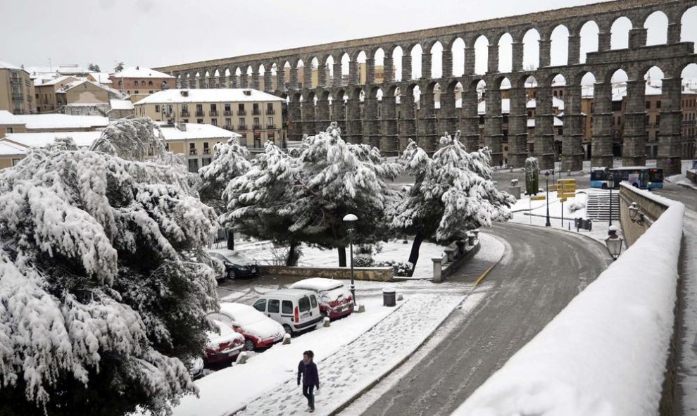 Una mujer camina por una calle junto al Acueducto de Segovia, que despertó hoy con una capa de más de diez centímetros de nieve. EFE/Aurelio Martín