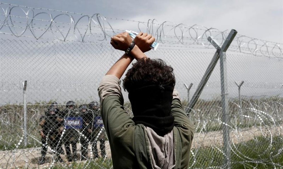 Un refugiado permanece tras la valla fronteriza frente a un grupo de policías macedonios durante una protesta en el campo de refugiados de Idomeni, situado en la frontera entre Macedonia y Grecia. EFE/Kostas Tsironis