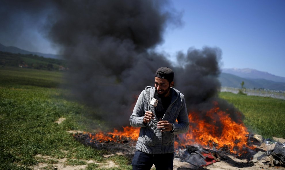 Un reportero de TV ejerce su trabajo mientras unas mantas arden cerca del ampo de refugiados de Idomeni, Grecia. REUTERS/Stoyan Nenov