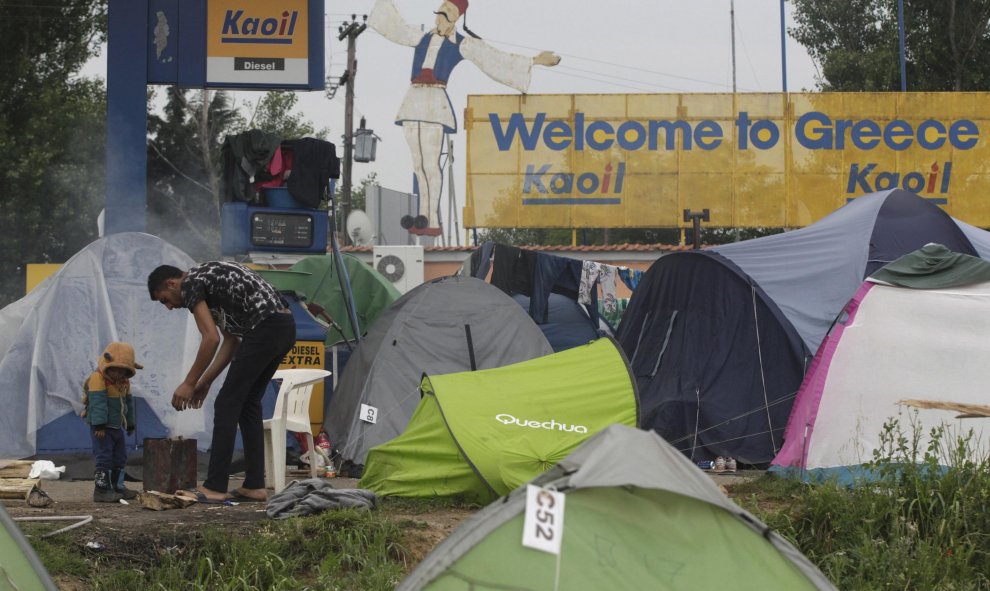 Un refugiado y su hui se calientan en una estufa improvisada junto a las tiendas del  campamento de Idomeni, en la frontera entre Grecia y Macedonia. REUTERS/Alexandros Avramidis