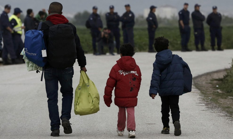 Un refugiado con sus hijos lleva sus pertenencias ante la mirada de los agentes de la policía helena  durante el desalojo del campamento de Idomeni, en la frontera entre Grecia y Macedonia. REUTERS/Yannis Kolesidis