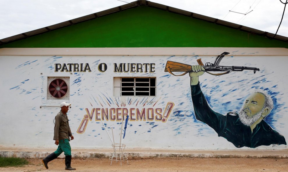 Un hombre pasa junto a un edificio en la localidad cubana de Bauta, en cuya fachada hay pintado un retrato de Fidel Castro con el lema 'Patria o Muerte ¡Venceremos!'. REUTERS/Stringer