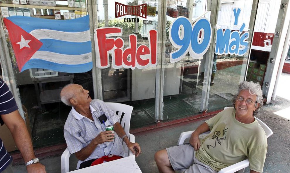 Unas personas toman cerveza junto a un anuncio alusivo al 90 cumpleaños del líder de la revolución cubana Fidel Castro. EFE/Ernesto Mastrascusa