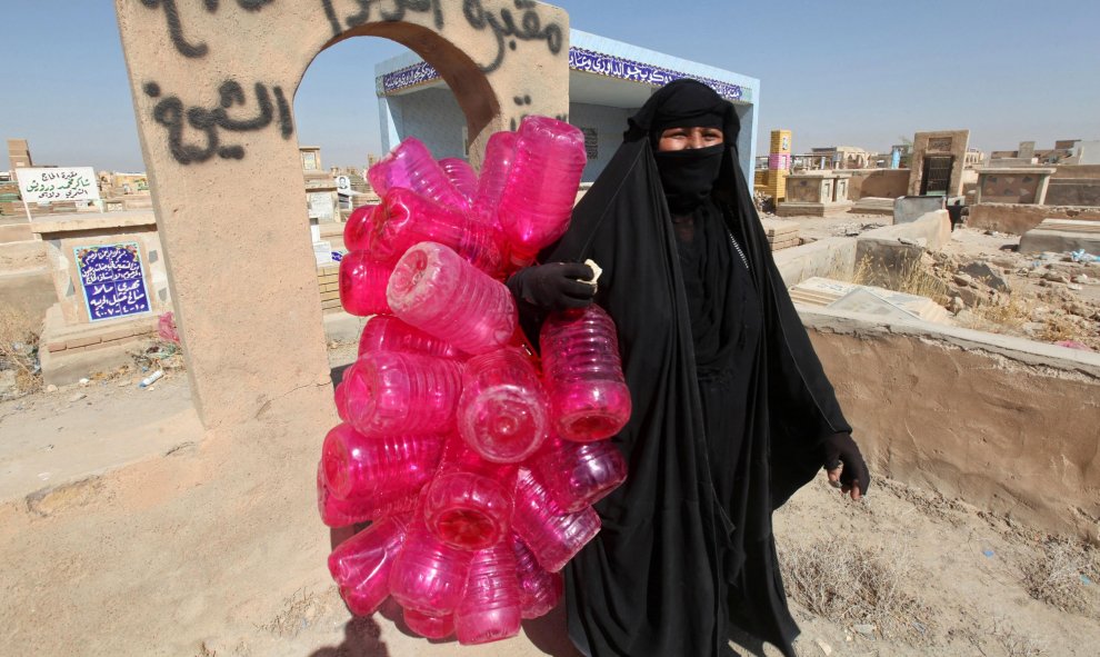 Una mujer lleva los bidones de agua que se emplean para limpiar las tumbas del  cementerio de Wadi al-Salam ('Valle de la Paz'), en Najaf, al sur de Bagdad. REUTERS/Alaa Al-Marjani