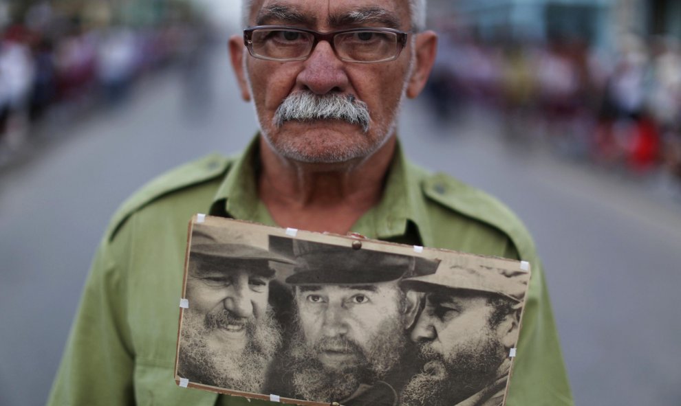 Un hombre sujeta fotografias de Fidel Castro mientras espera la caravana con las cenizas del exmandatario cubano. REUTERS