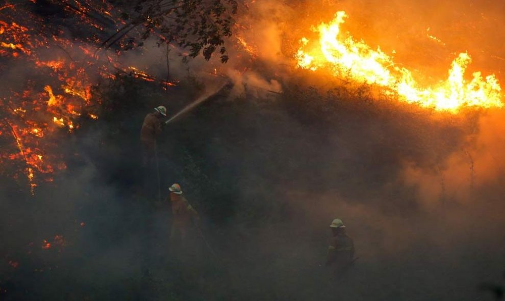 Varios bomberos utilizan las mangueras para contener el fuego en los alrededores del pueblo de Fato. | RAFAEL MARCHANTE (EFE)