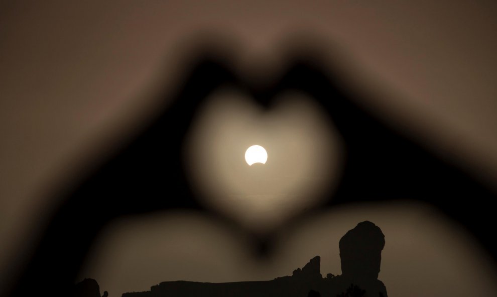 Una mujer hace el gesto del corazón con las manos enmarcando el eclipse de Sol, en el Roque Nublo, en Gran Canaria. REUTERS/Borja Suarez