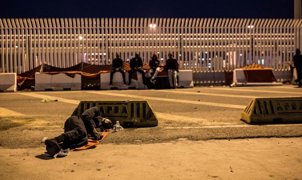 Un migrante duerme en el suelo del puerto del Algeciras, junto a más de 170 personas rescatadas por Salvamento Marítimo durante el fin de semana. JAIRO VARGAS