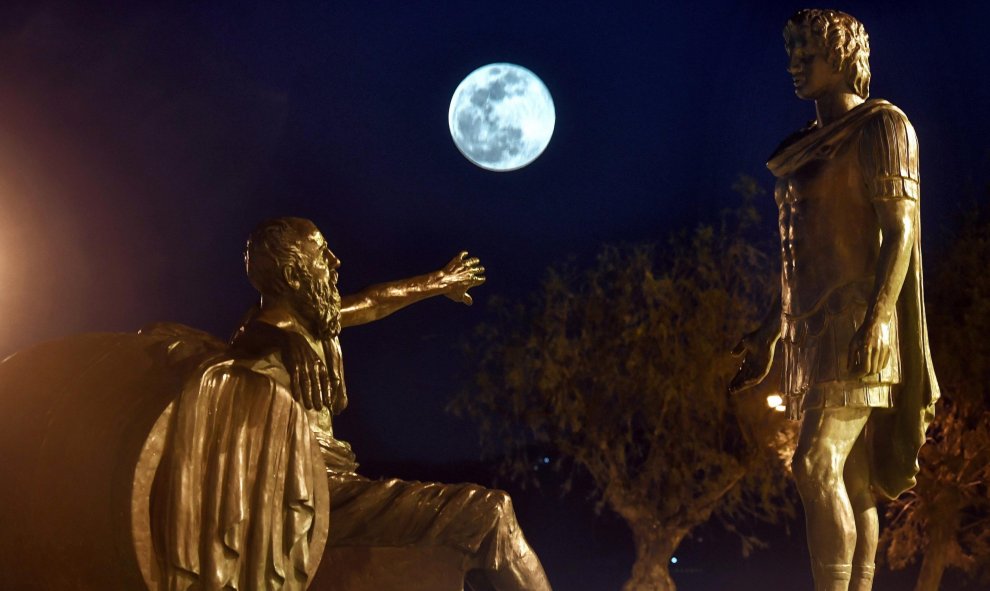 Vista de la luna de nieve, detrás de estatuas del antiguo filósofo cínico griego Diogenes, y el antiguo rey macedonio griego Alejandro Magno en la ciudad de Corinto, Peloponeso | EFE/Vassilis Psomas