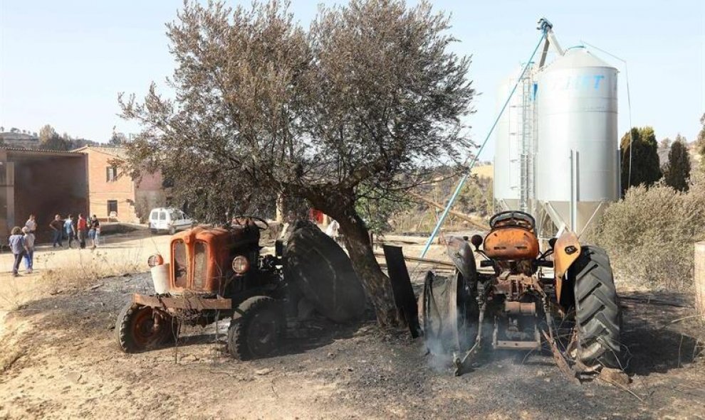 Unos tractores afectados en una granja por el incendio forestal que quema desde la tarde de ayer en varios términos municipales de la comarca tarraconense de Ribera d'Ebre, y que sigue descontrolado y afecta ya a más de 4.000 hectáreas.EFE/ Jaume Sellart